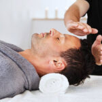 New age practitioner directs energy towards a young man's head. Horizontal shot.