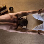 The man has massage - stretching move. Towel setup with spa flowers.