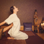 istockphoto-636568148-612x612 Professional thai masseuse is stretching female body. She is raising leg to her back. Young woman is sitting on floor. Her eyes are closed with pleasure